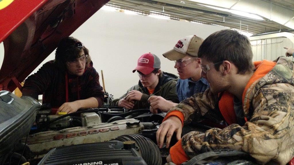 Teacher talking to students under the hood of a vehicle