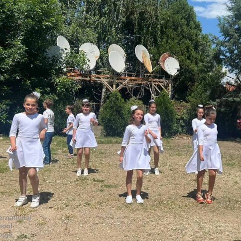 Children in white dresses performing an outdoor dance