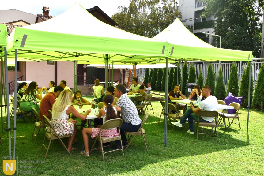 Families dining under green tents at the BBQ social