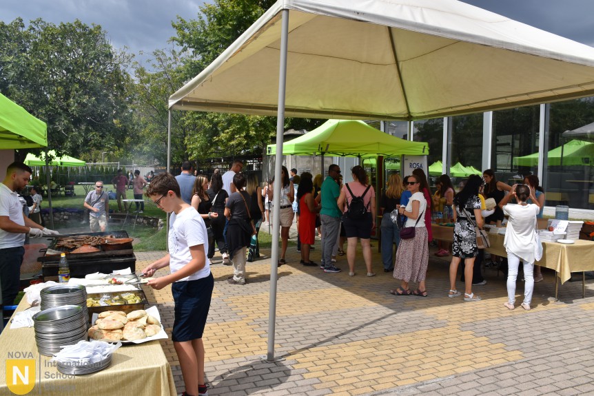 Families lining up at the grill under a tent at the BBQ social