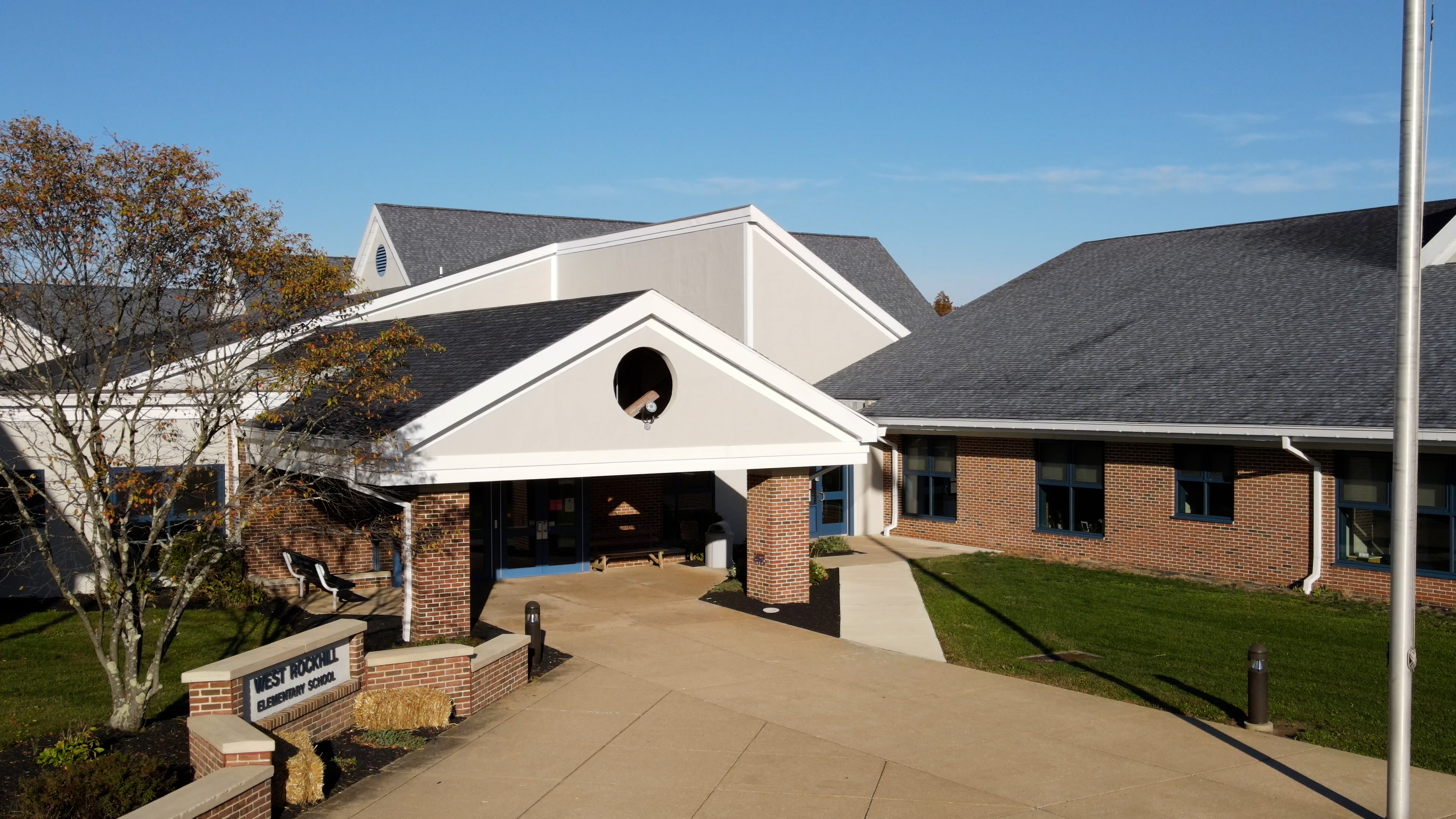 A brick and stone building with a peaked roof and an arched entryway, surrounded by a paved walkway and landscaped grounds.
