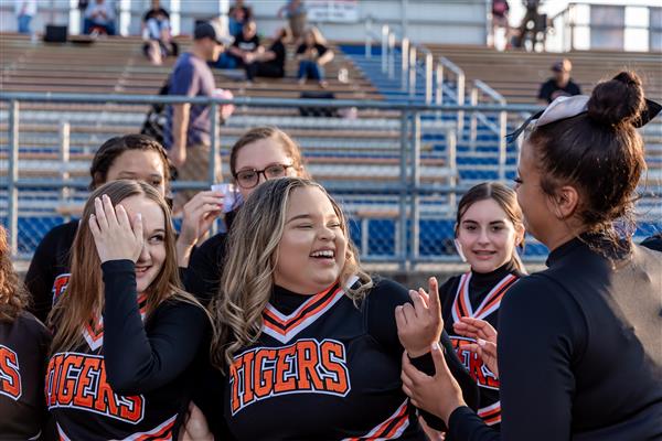 group of cheerleaders dancing and laughing with bleachers in background