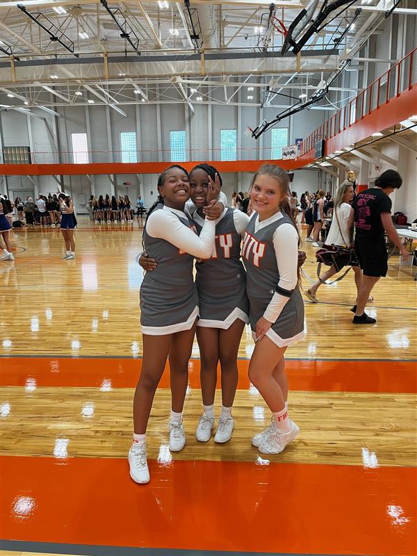 three cheerleaders in gray uniforms in gym