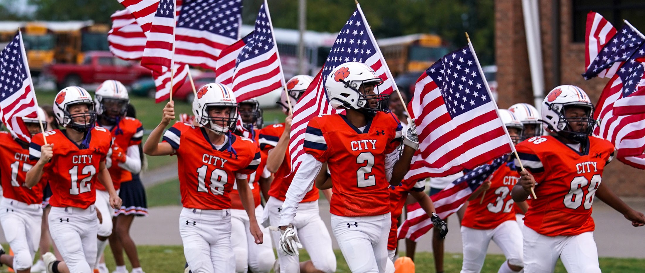 football players in orange holding US flags running onto field