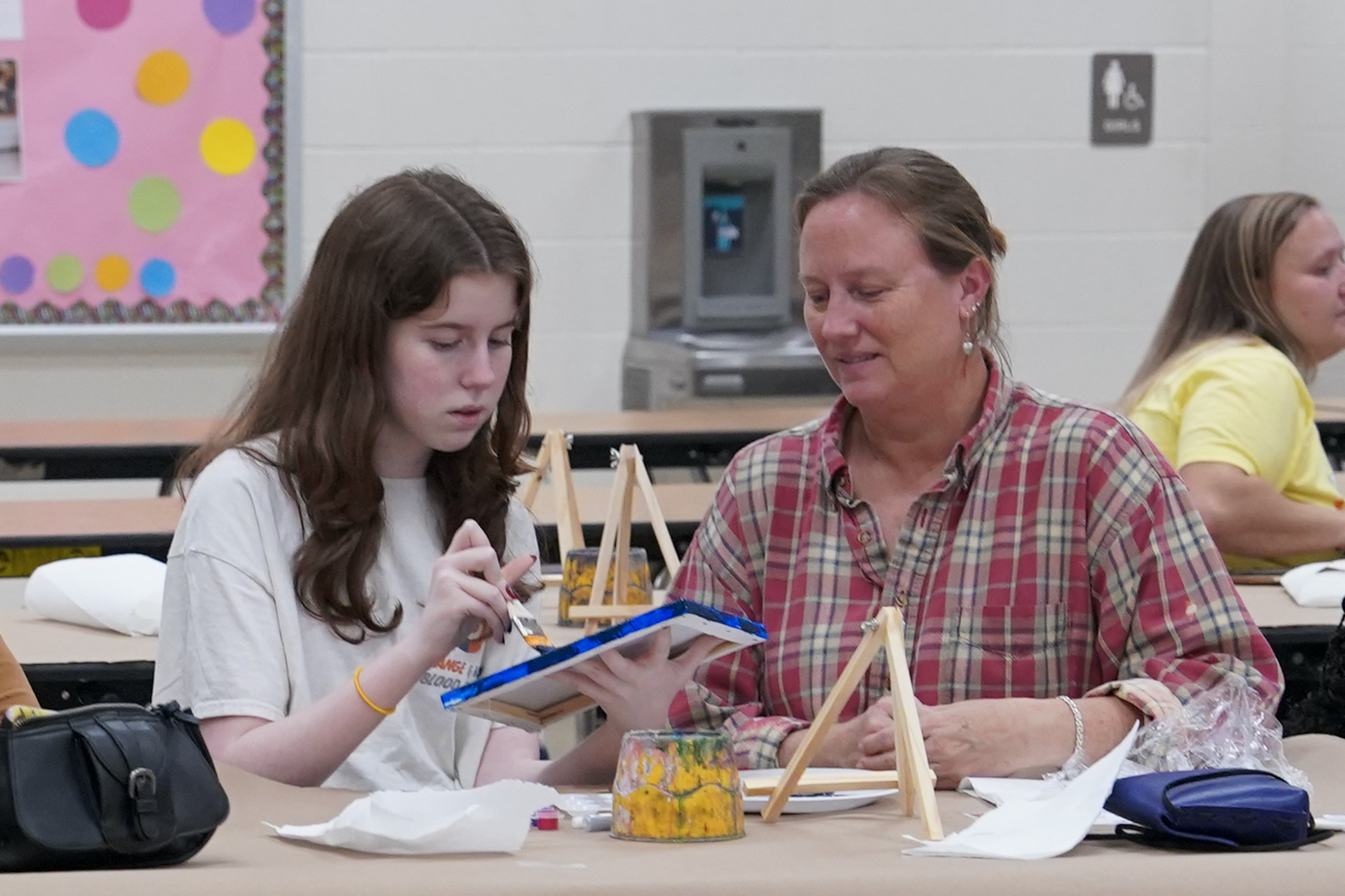 Student seated at table painting on canvas