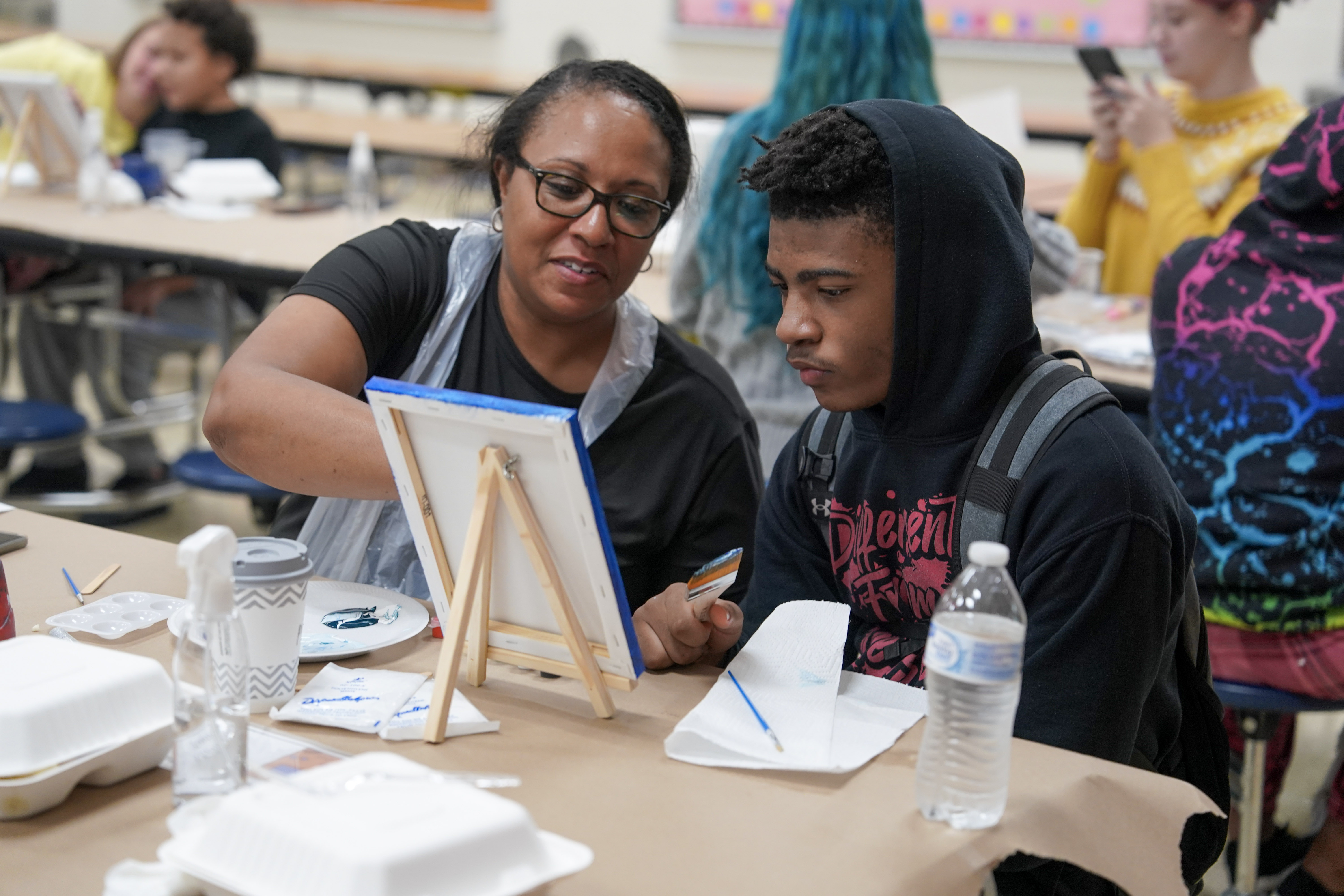 Student seated at table painting on canvas