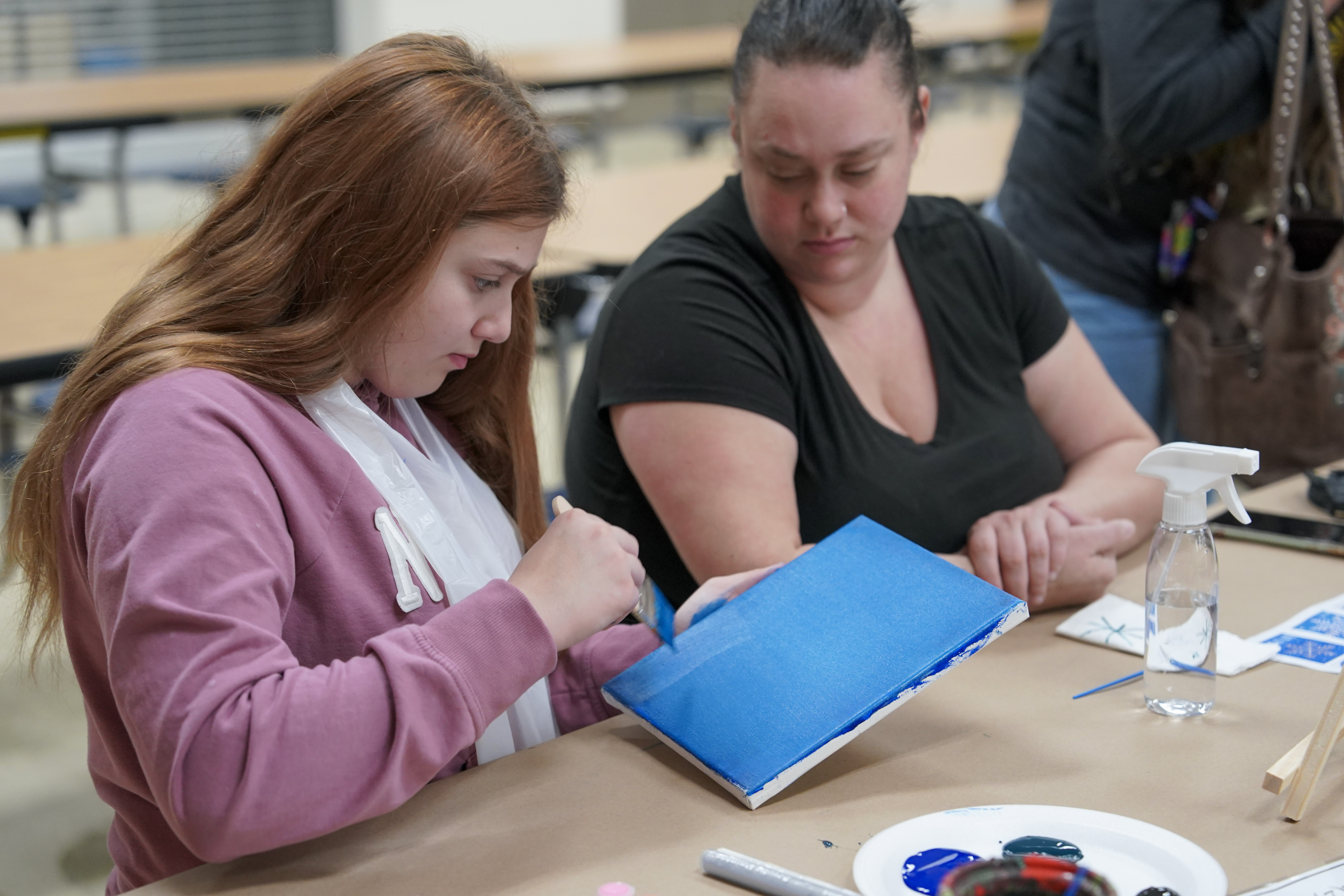 Student seated at table painting on canvas