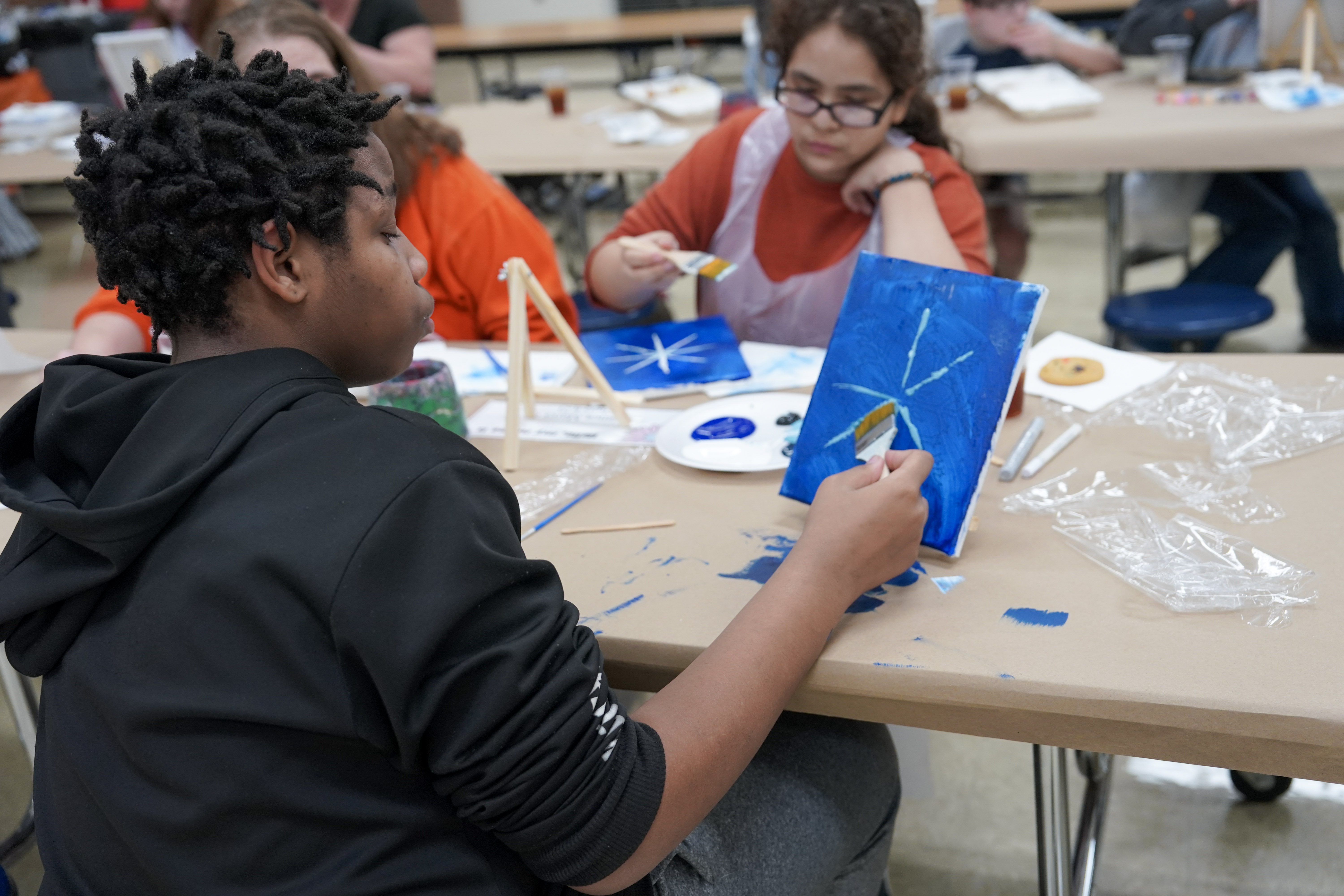 Student seated at table painting on canvas