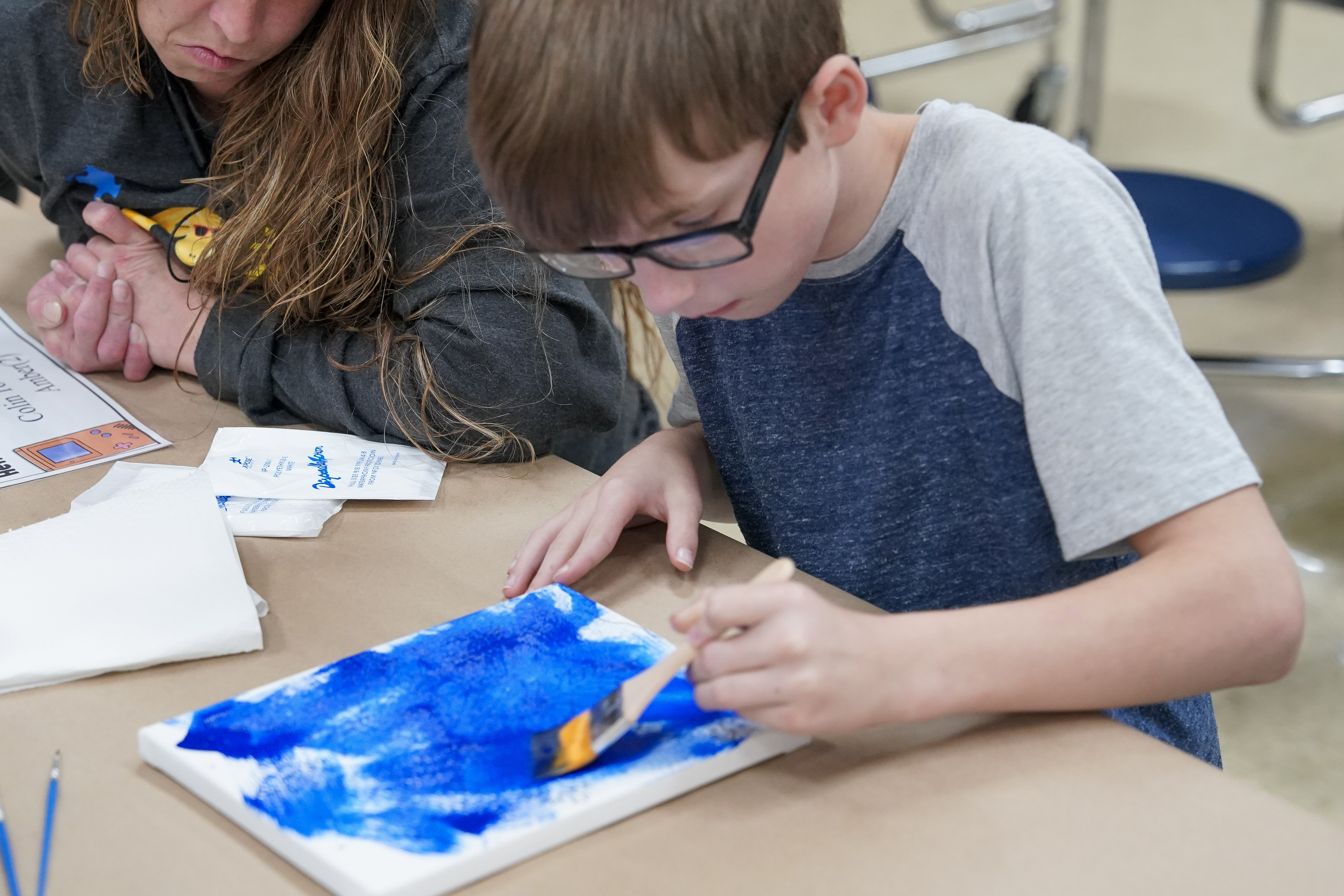 Student seated at table painting on canvas