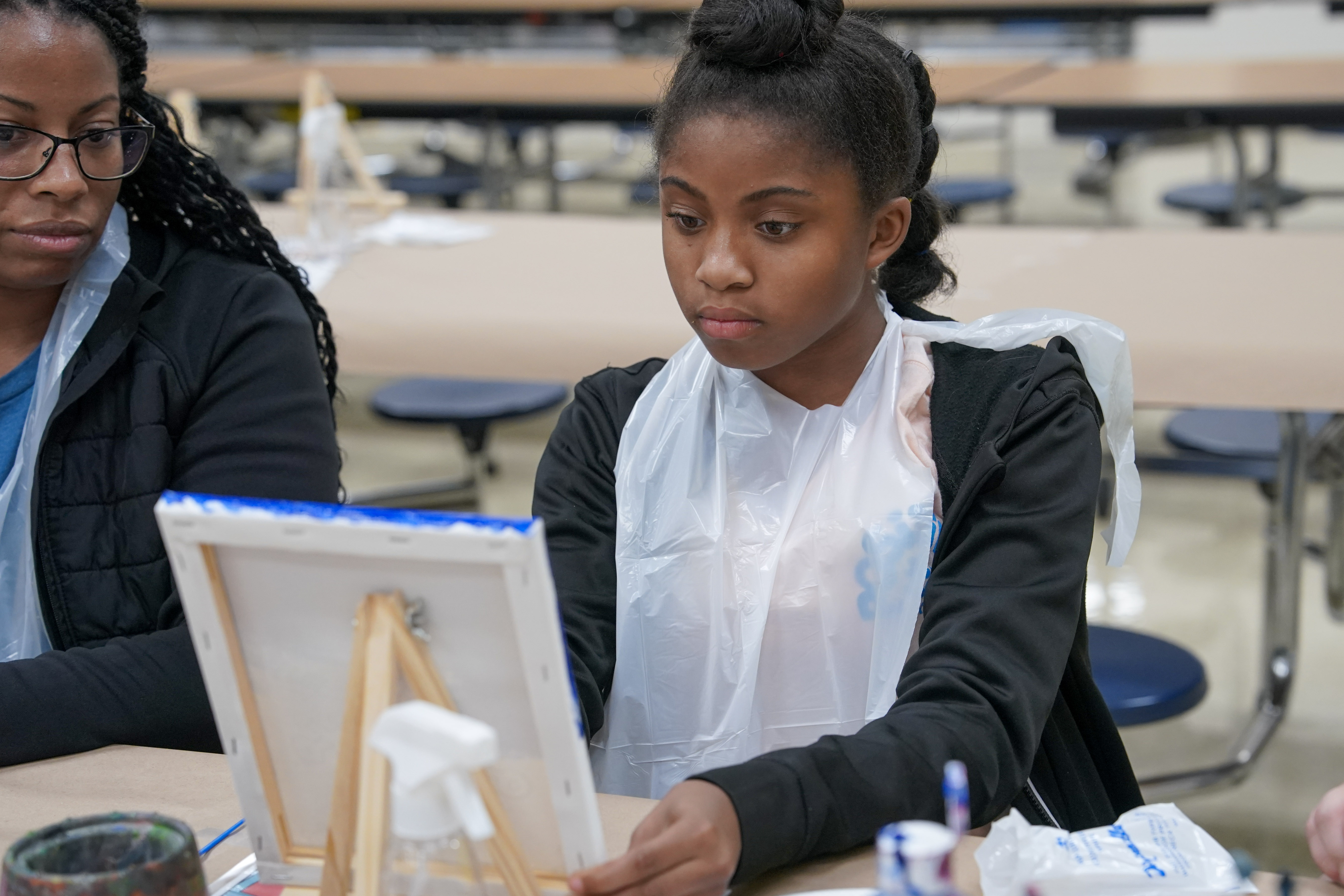 Student seated at table painting on canvas 