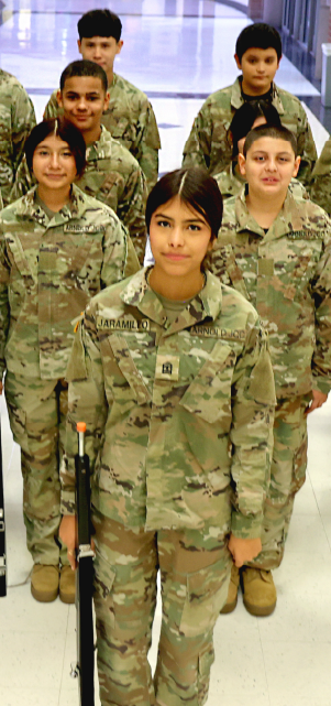 A group of young individuals wearing military-style camouflage uniforms, standing together in what appears to be a military or training facility.