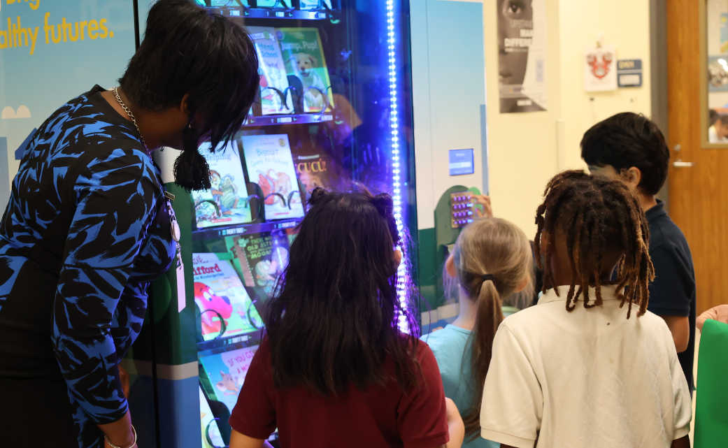 The image shows several people, including a person wearing a patterned jacket, standing in front of a vending machine in what appears to be a hallway or corridor.