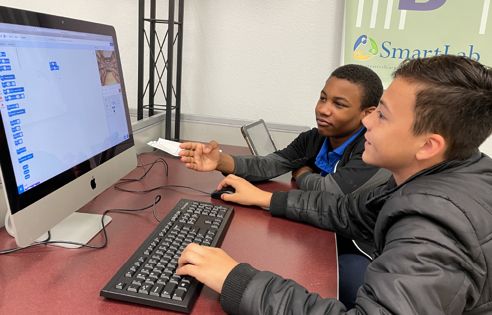 Two young boys are sitting at a computer, intently focused on the screen as they interact with the keyboard and mouse.