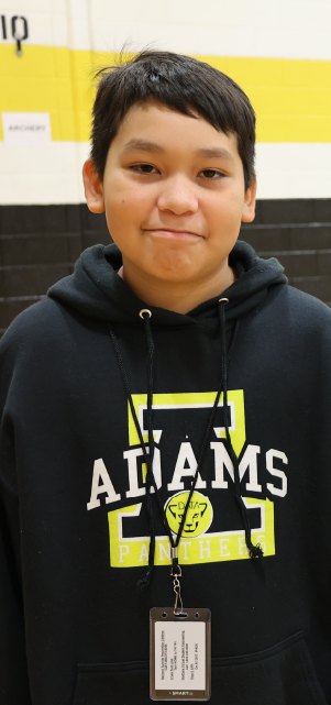 A young person wearing a black hoodie with the text "ADAMS" printed on it, standing in front of a yellow background.