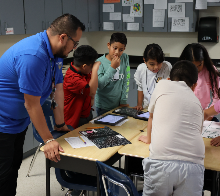 A group of students and a teacher are gathered around a table, engaged in a collaborative learning activity in a classroom setting.