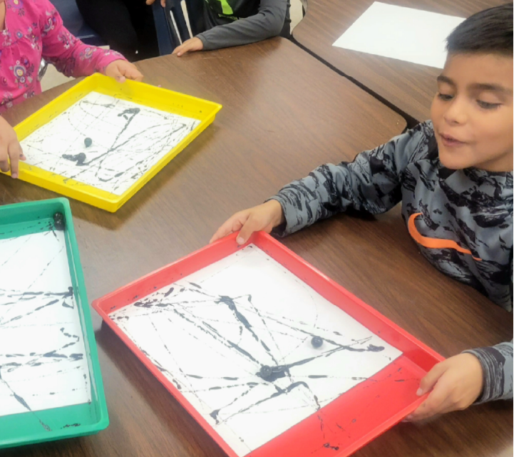 A young child is intently focused on creating art using a frame and various materials on a table.