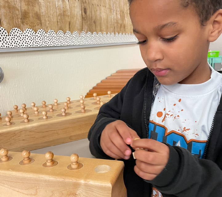 A young boy is intently focused on playing chess, with a wooden chessboard and pieces visible in the foreground, and a wooden wall with decorative elements in the background.