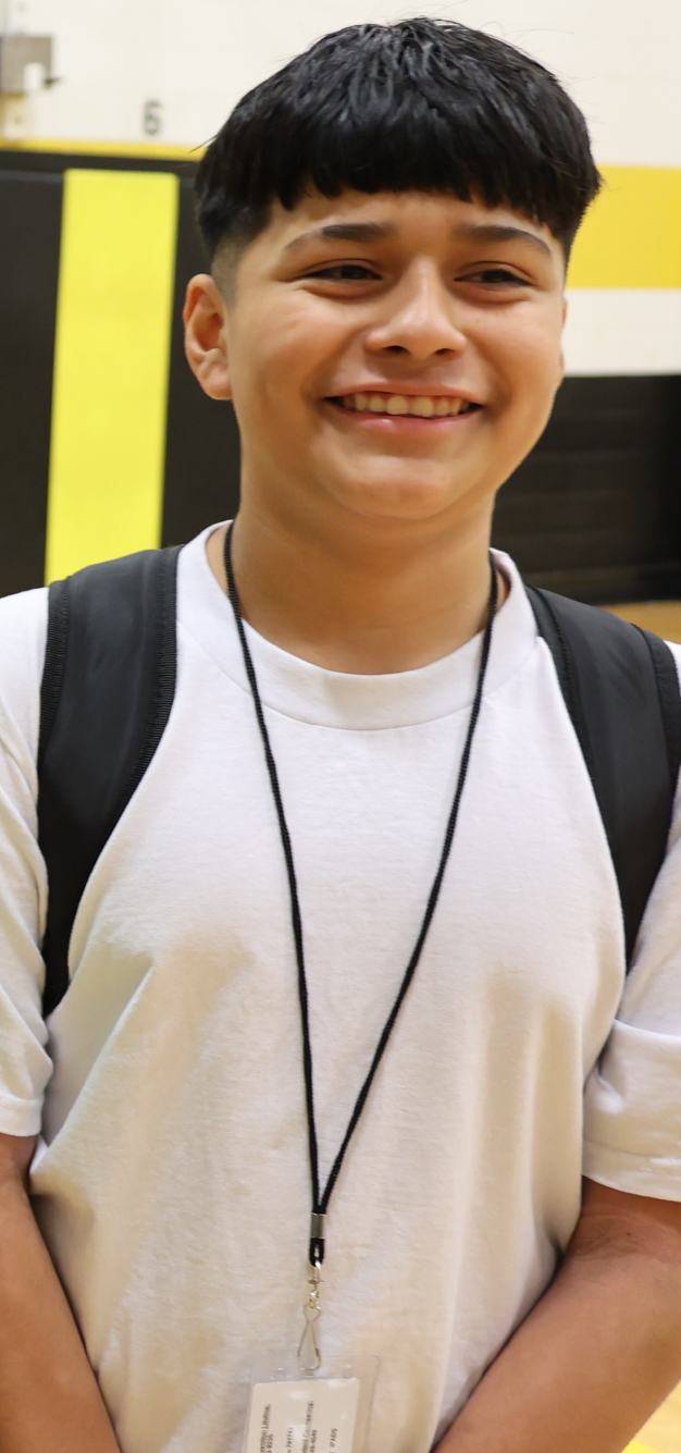 A smiling young person wearing a white shirt and backpack stands in front of a yellow background.