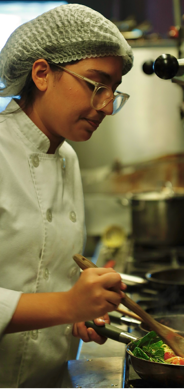 A person in a chef's uniform is carefully preparing a dish in a kitchen setting.