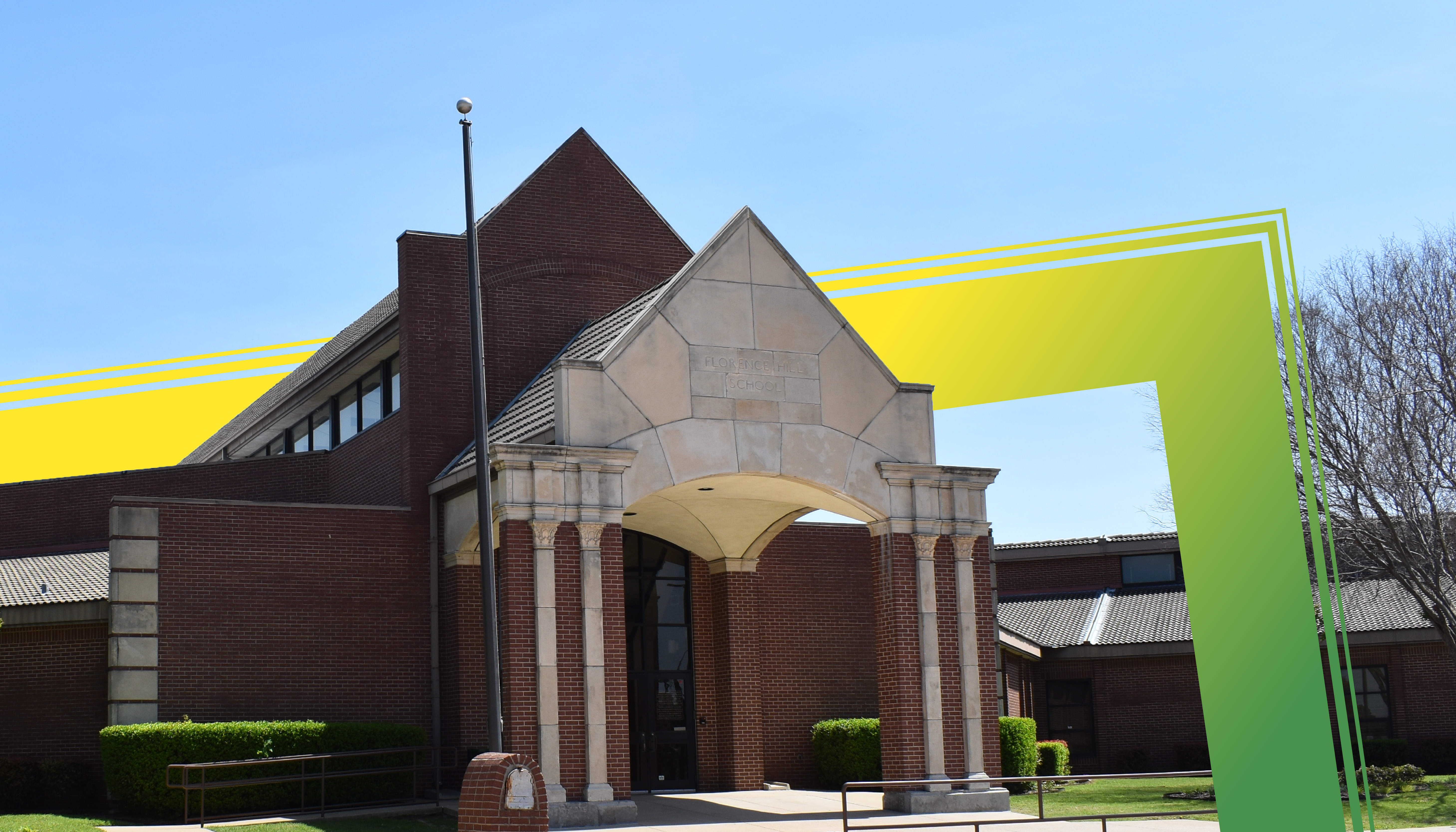 A brick building with an arched entryway and a yellow and green geometric structure in the foreground against a clear blue sky.
