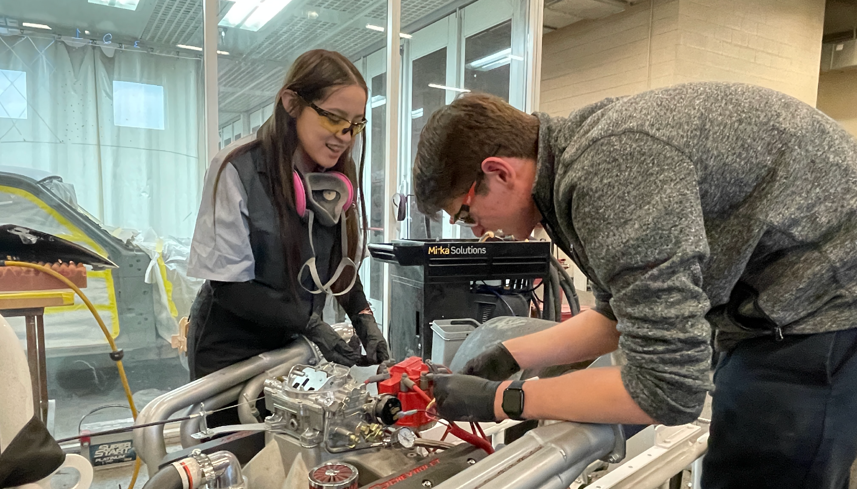 Two individuals are working on a mechanical device, with one person closely examining the internal components while the other provides assistance.