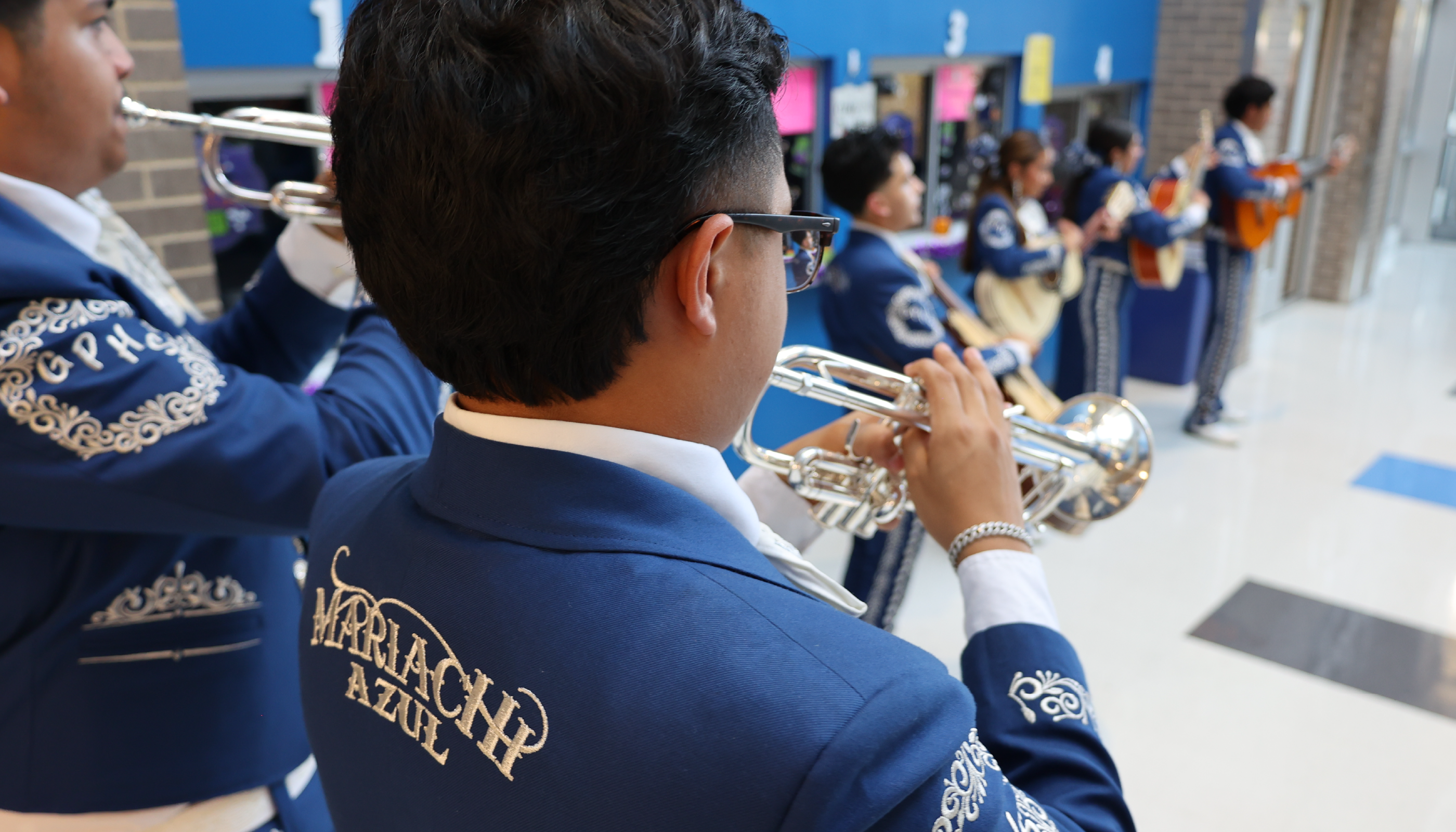 A person in a blue uniform with a musical instrument is standing in a crowded hallway with other people in similar uniforms.