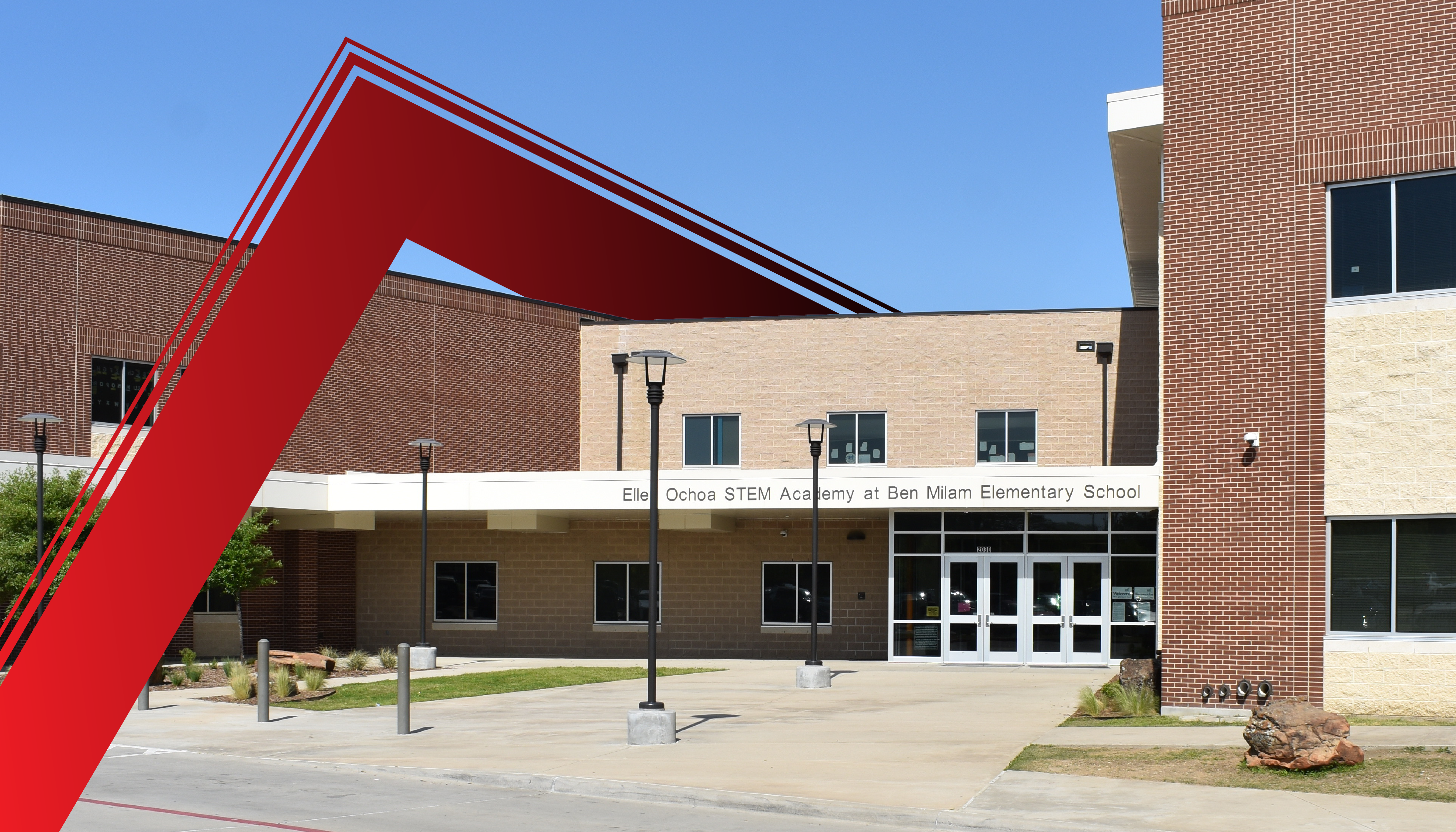 A large red triangular structure stands in the foreground, framing the entrance of a brick building with glass windows and doors in the background.