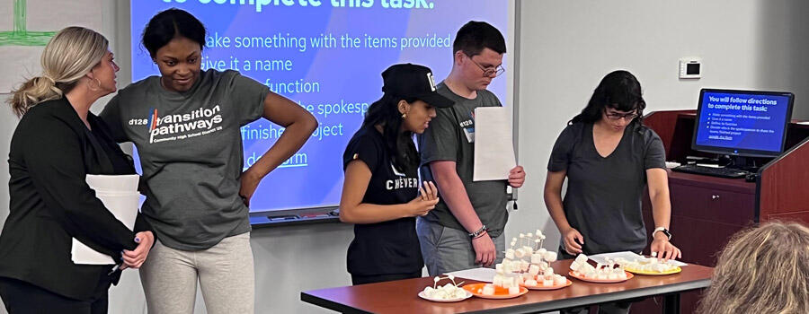 Two teachers standing near three students giving a class presentation