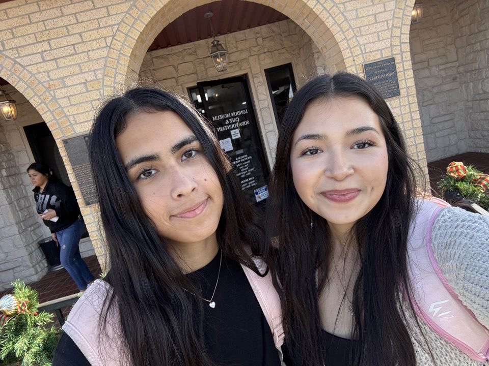 Two students with backpacks on in front of a school