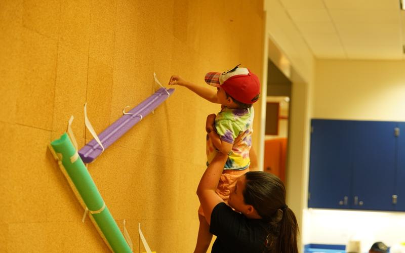 Mom holds young boy up to reach exhibit at STEMfest 2024