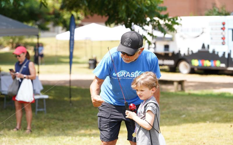 A man teaches a young boy to fish at STEMfest 2024
