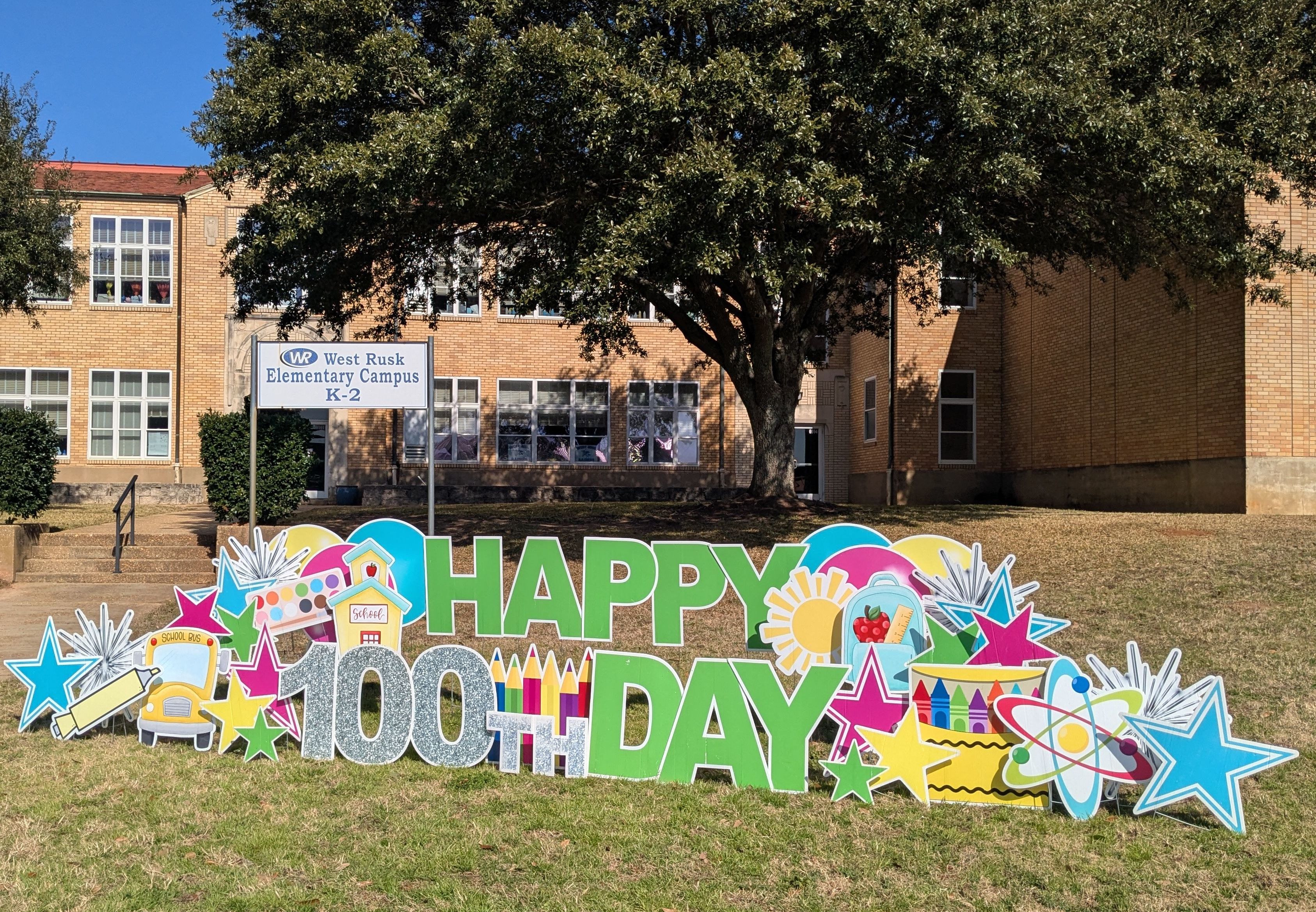 The words "happy 100th day" with stars and balloons in front of the Elementary Building