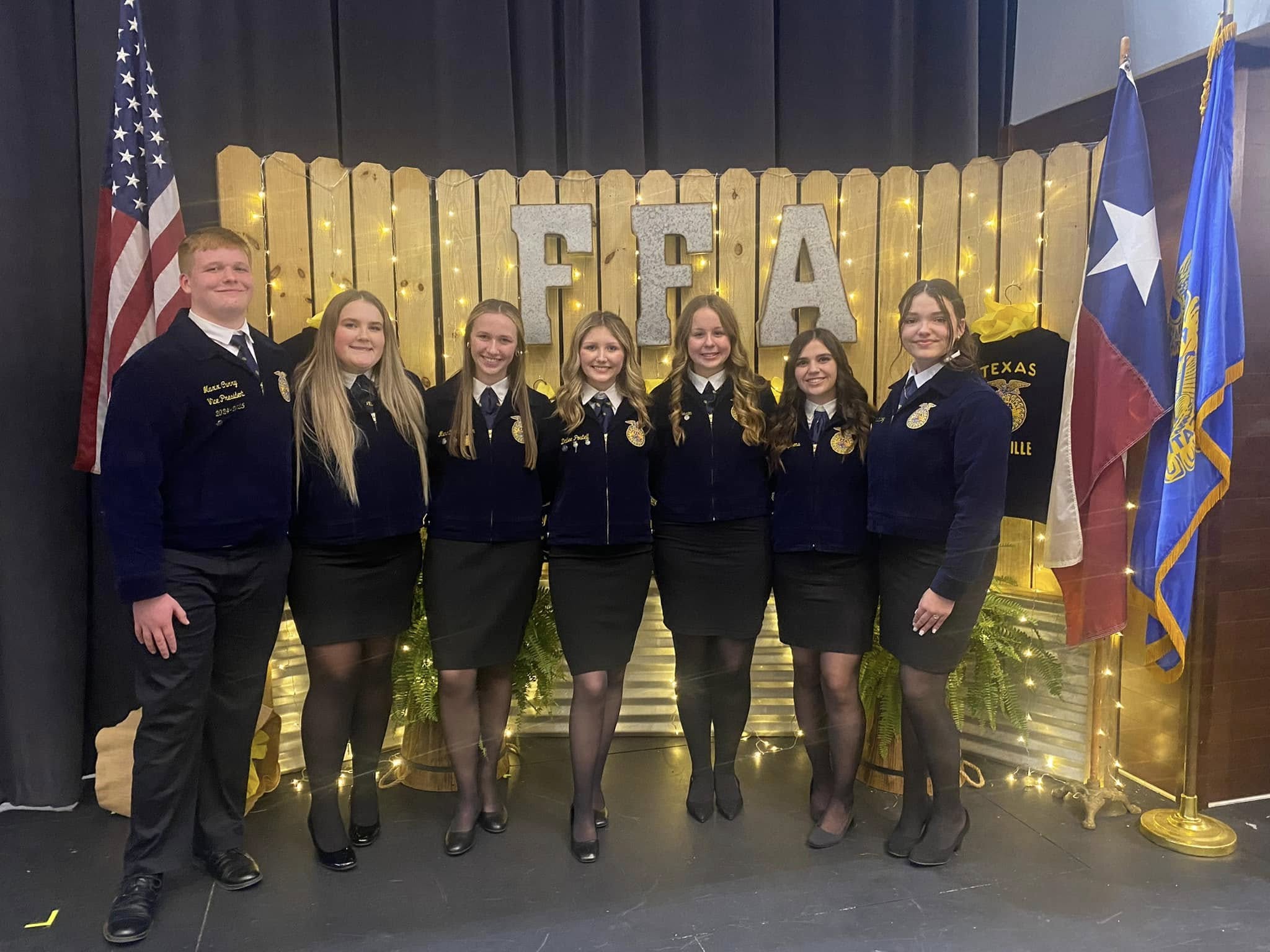 A young man and 6 young women standing in between two flags as Ag officers