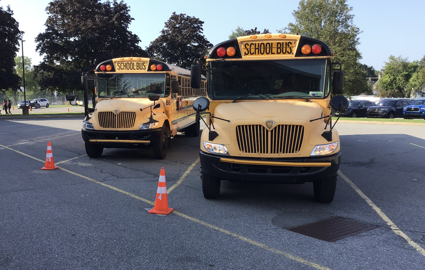Two orange school buses are lined up in front of the school on a sunny day.