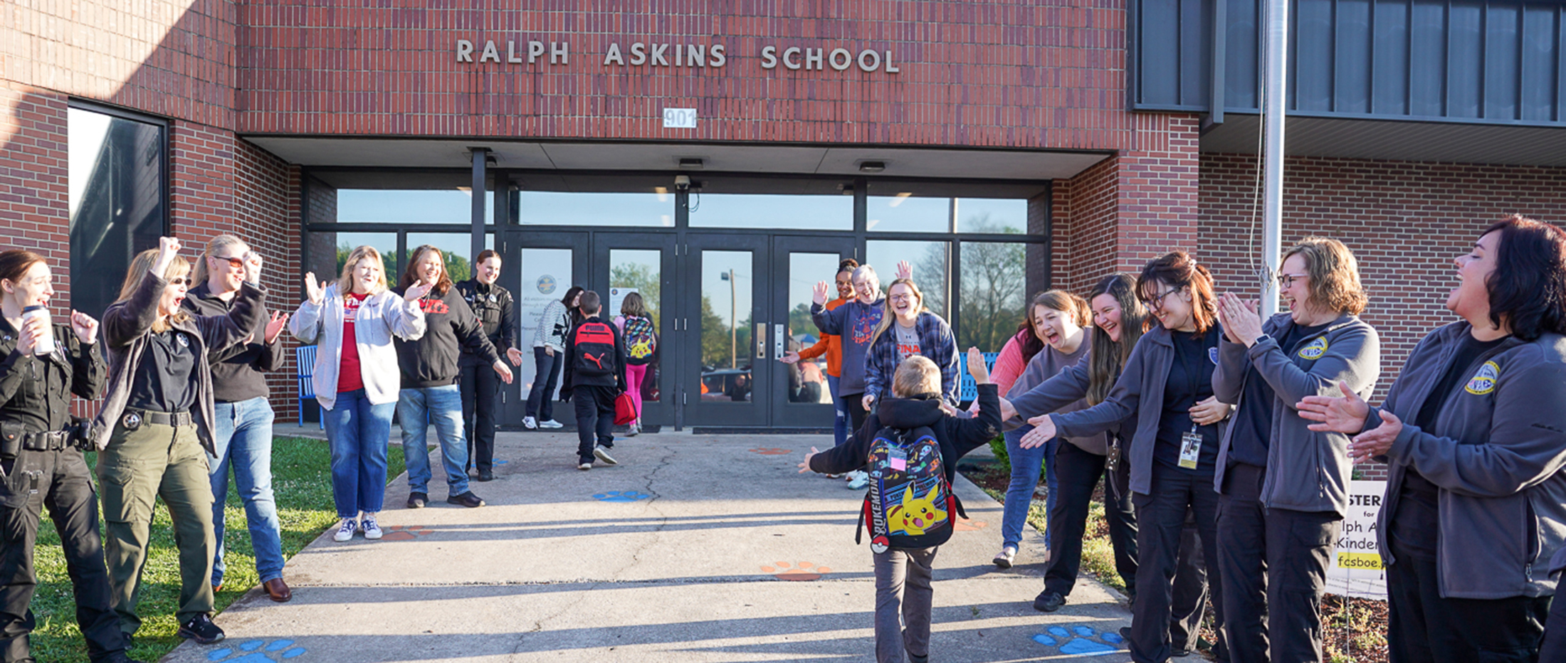 group of ladies greeting young student in front of school