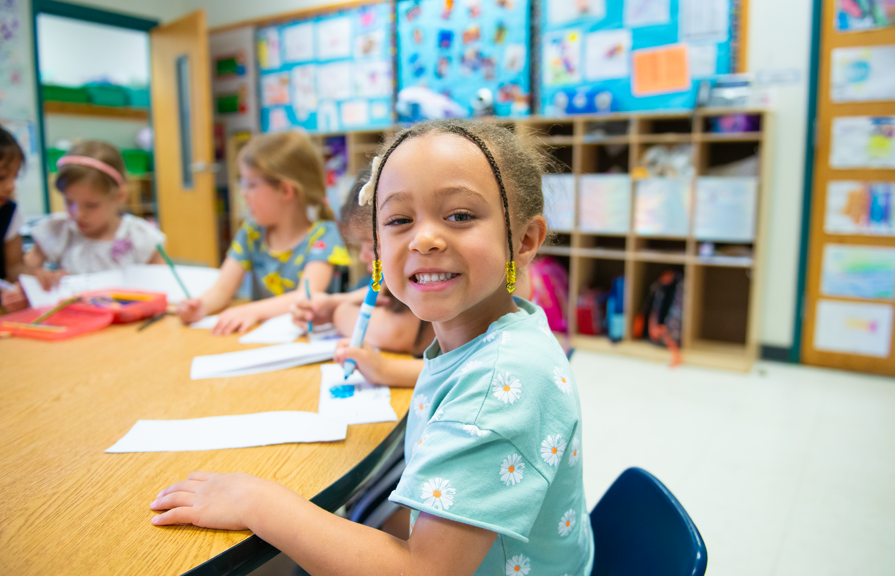 little girl drawing with a blue marker at a desk