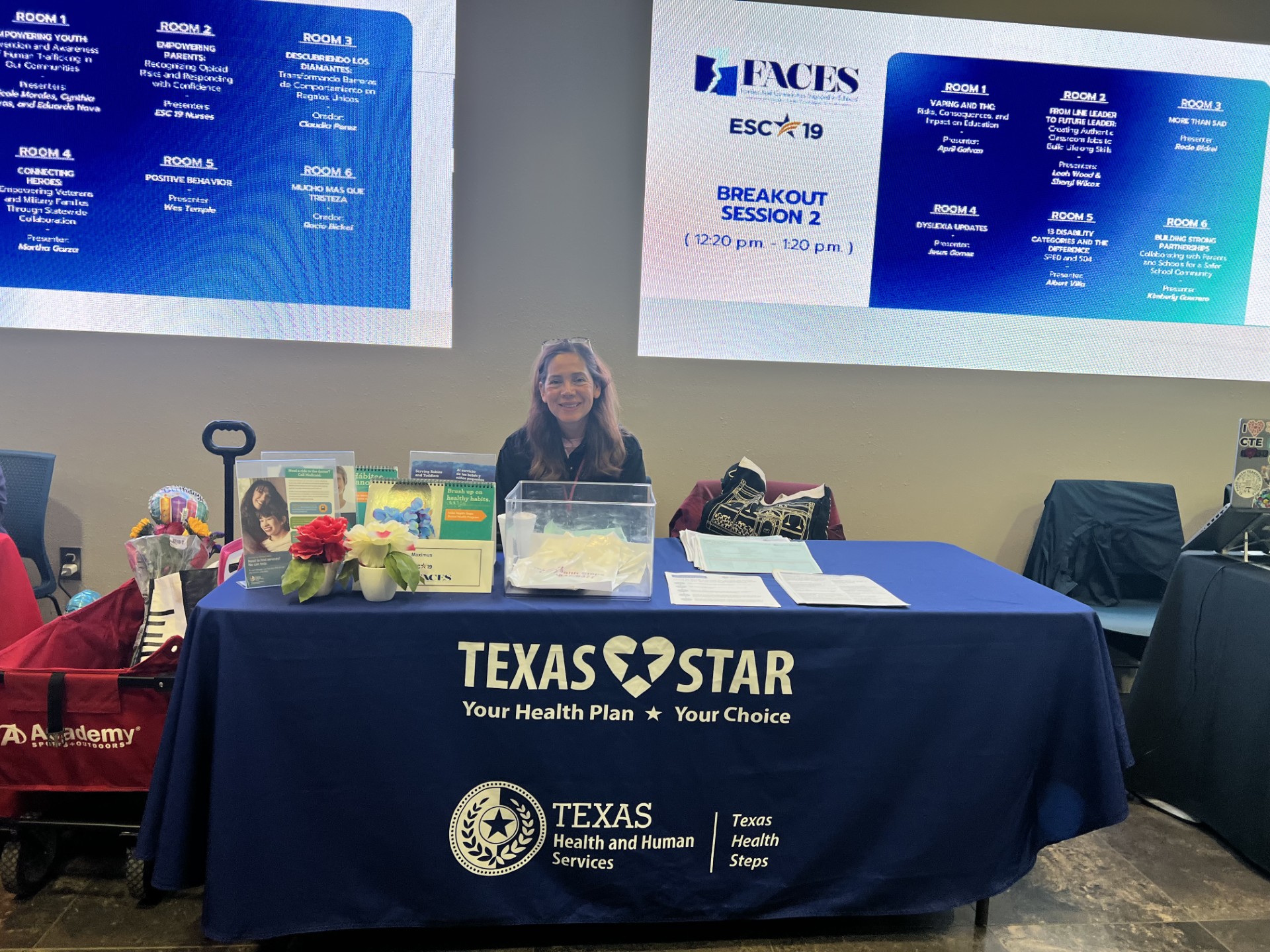 A woman smiles from behind a table with "Texas Star" branding, while large screens displaying event schedules hang in the background.