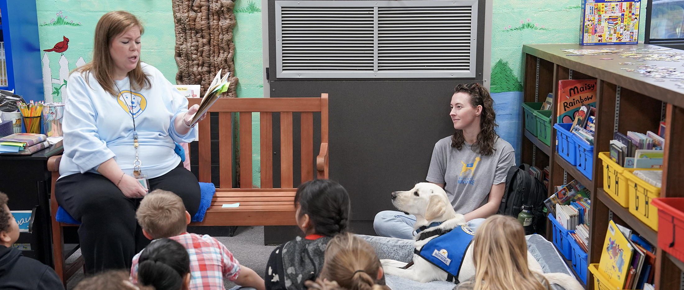 Henry the facility dog and students listening to a woman read a book