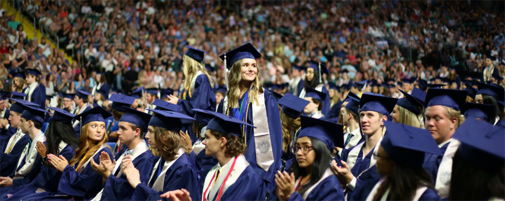 A large crowd of graduates in blue graduation gowns and caps, gathered together to celebrate their academic achievement.
