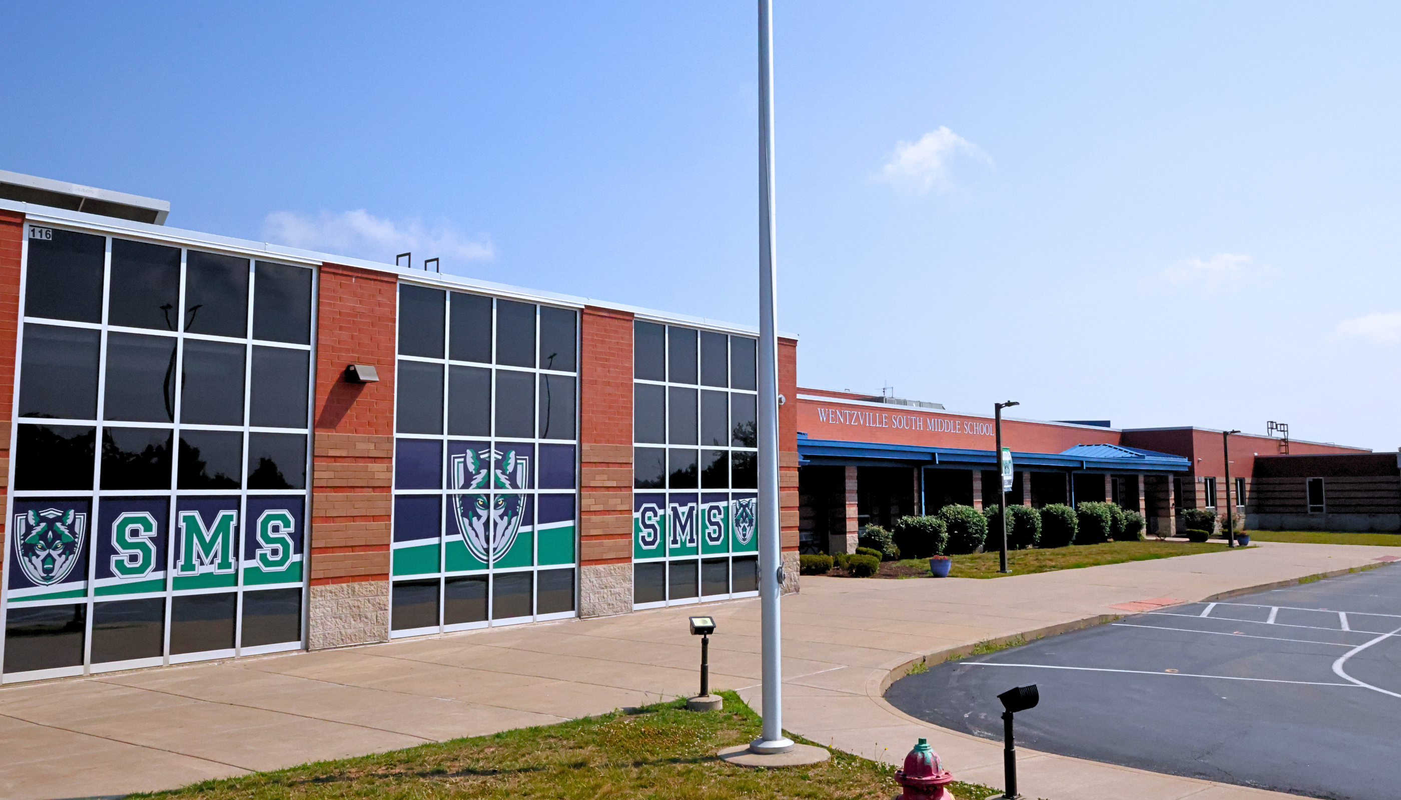 A large commercial building with a glass facade and the letters "SMS" prominently displayed, surrounded by a paved parking lot and landscaping.