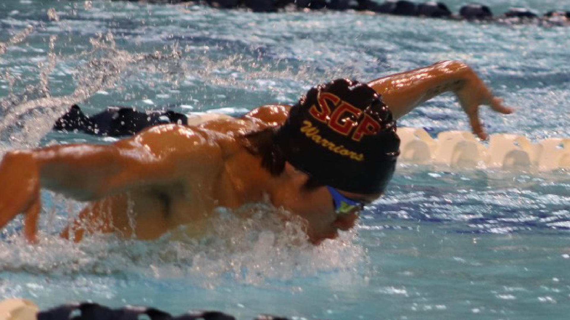 A person wearing a colorful swimsuit is swimming in a body of water, with waves and splashes visible in the background.