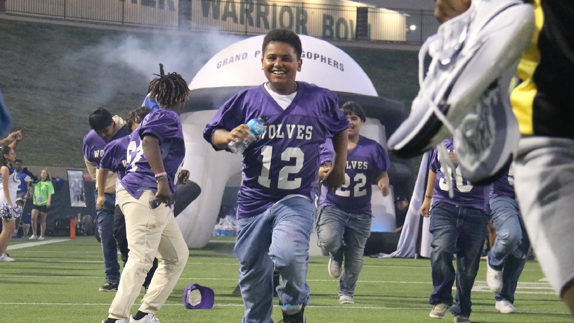 The image shows a group of people wearing purple uniforms and walking onto a sports field, with a large banner in the background displaying the team name "Wolves".