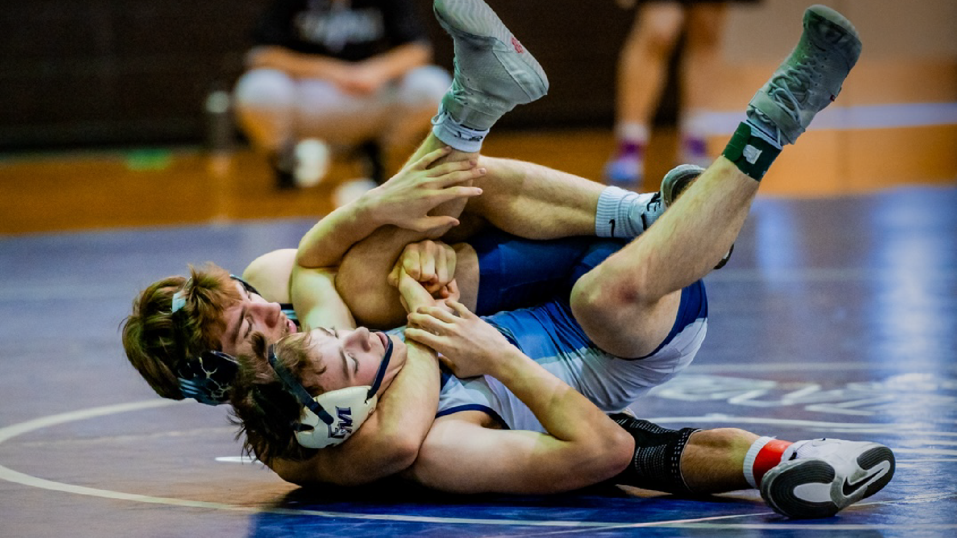 Two wrestlers engaged in a grappling match on a wrestling mat, with one wrestler attempting to pin the other to the ground.