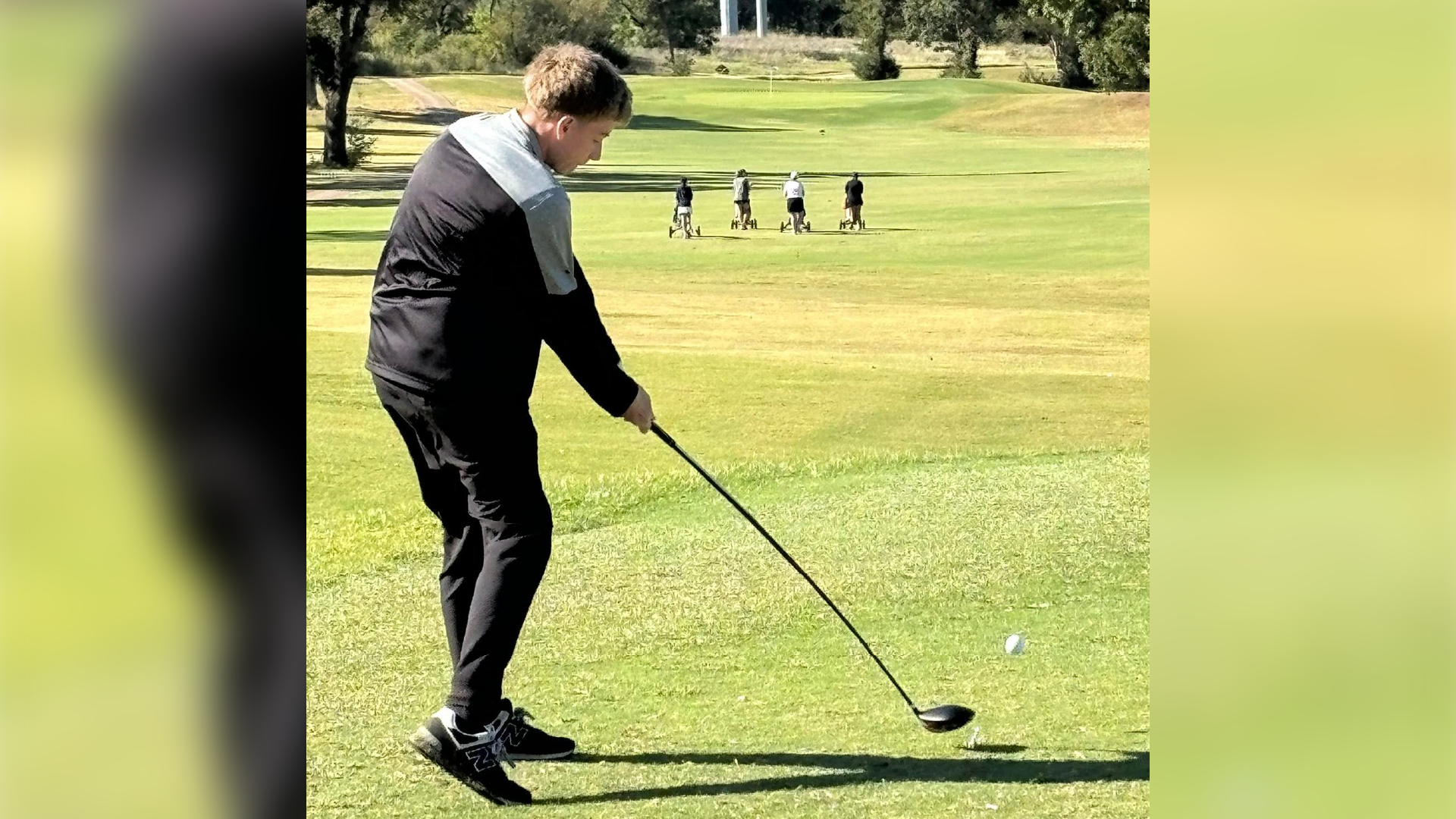 A man in a suit is standing on a golf course, preparing to take a swing with a golf club.