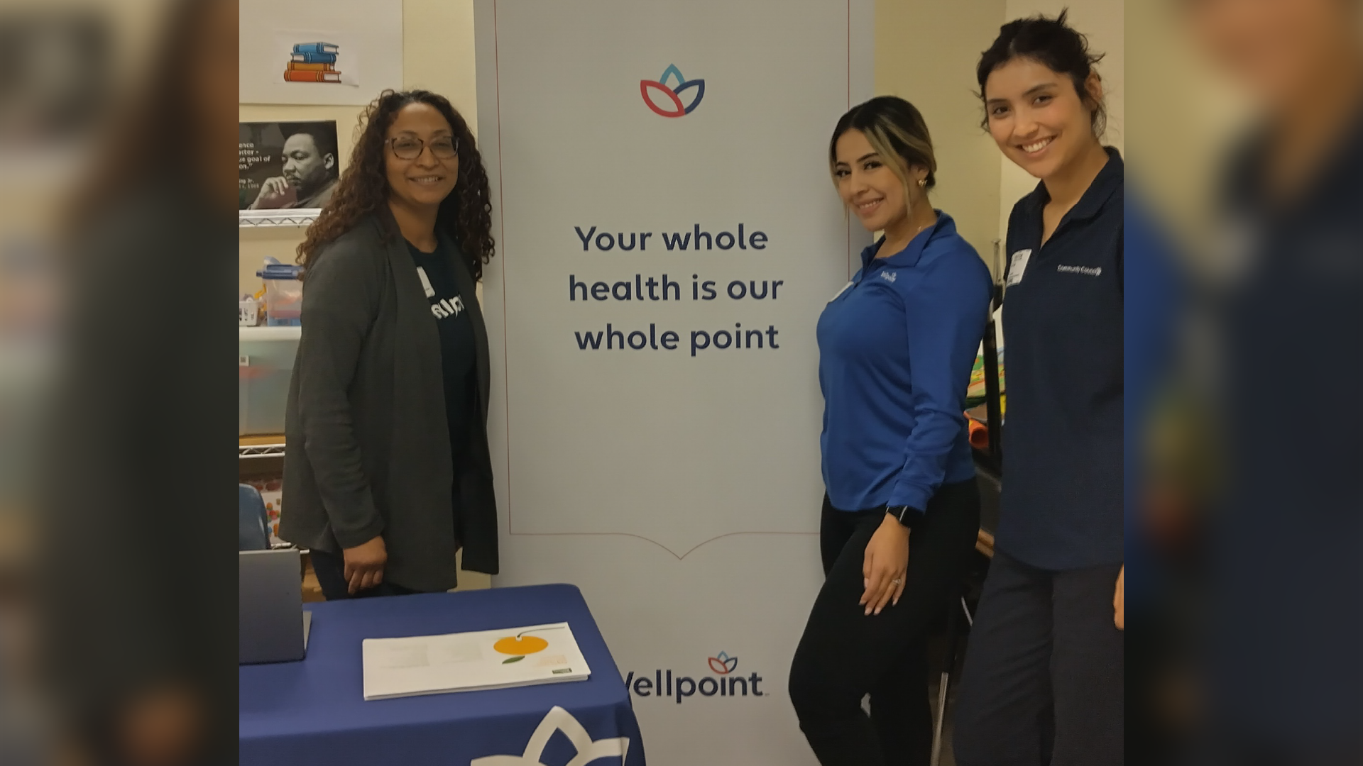 The image shows three women standing in front of a sign that says "Your whole health is our whole point", with the Wellpoint logo visible in the background.