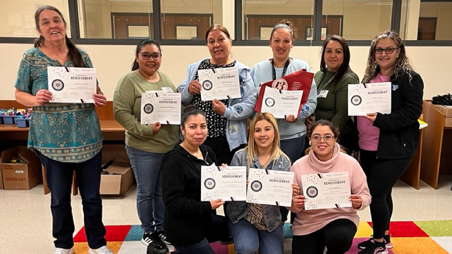 A group of people, likely students or teachers, are holding up certificates or awards in a classroom or school setting.