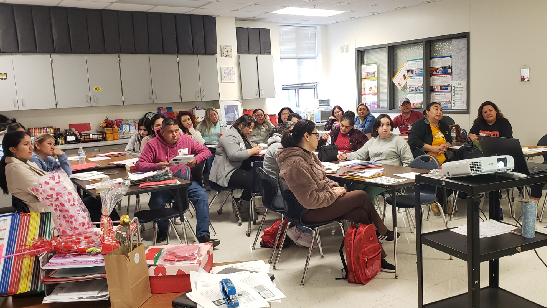 A crowded classroom filled with students sitting at desks, engaged in various activities and discussions.