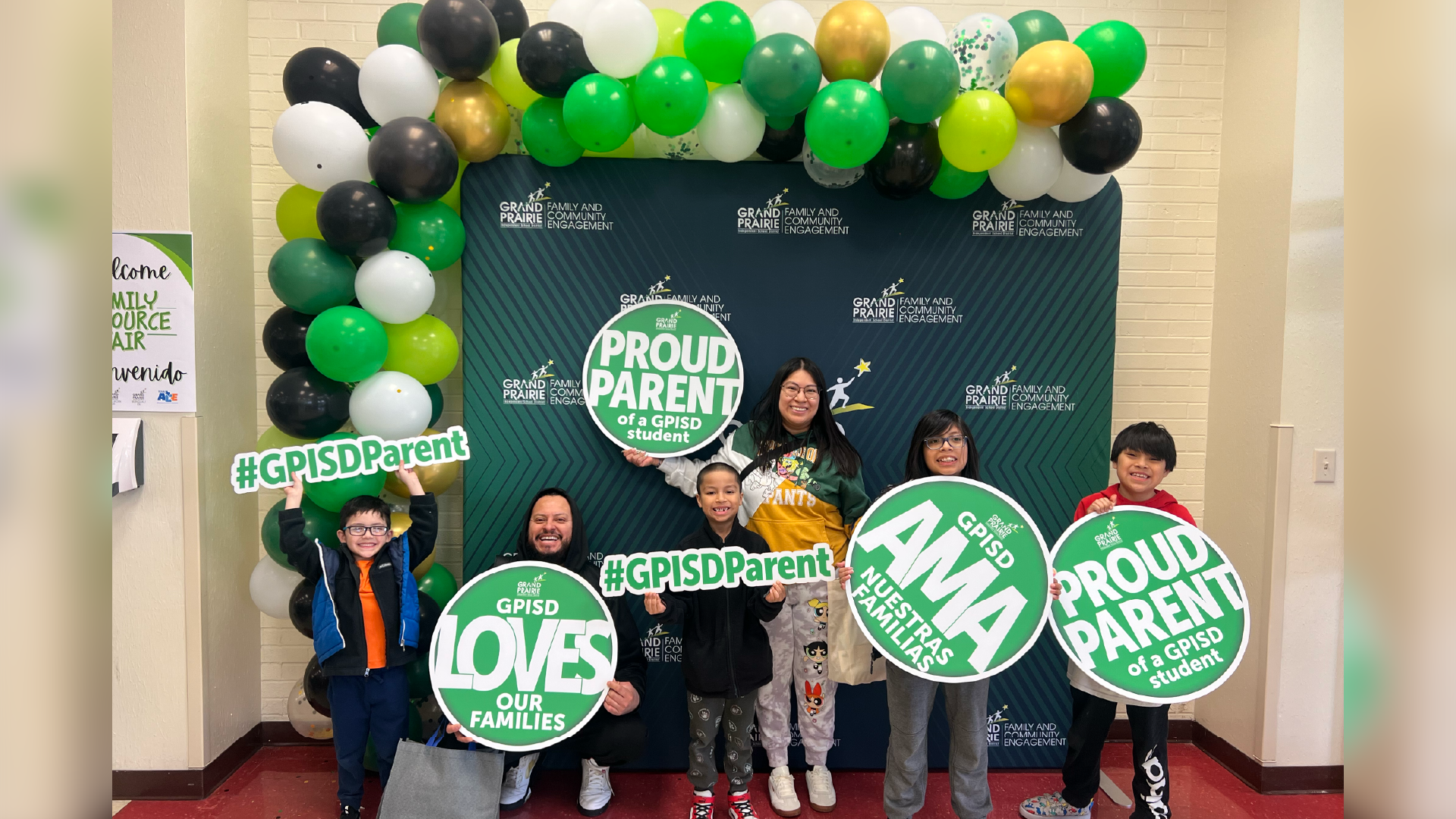 The image shows a group of people standing in front of a backdrop with balloons and text promoting "Proud Parents" and "#GPSD Parents".