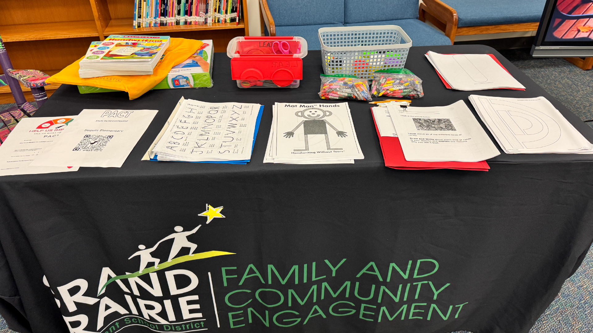 A table with various educational materials, including worksheets, books, and toys, along with a banner promoting "Family and Community Engagement" in the foreground.