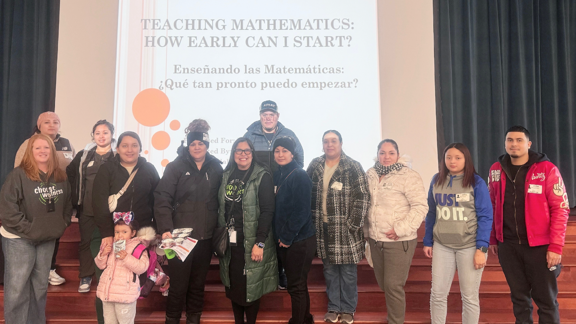 A group of people, mostly women, standing in front of a presentation slide titled "Teaching Mathematics: How Early Can I Start?" in both English and Spanish.